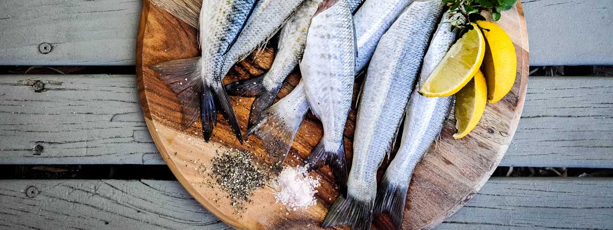 Ein Holzteller mit frischem Fisch, Salz, Pfeffer und Zitrone.